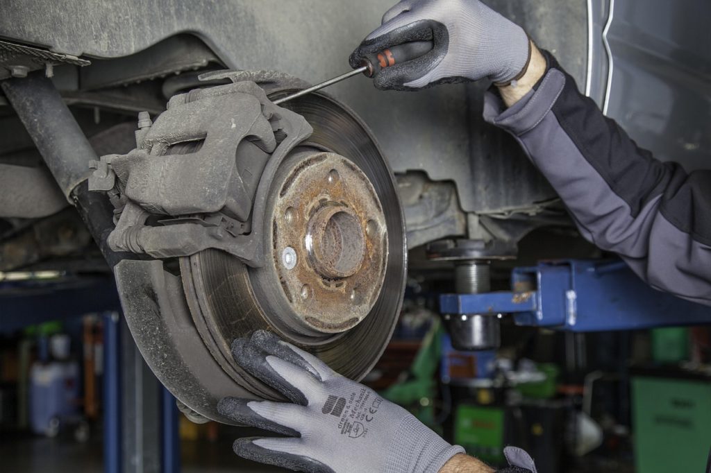 A man in a black shirt and gloves performs brake service on a car in a professional garage setting.